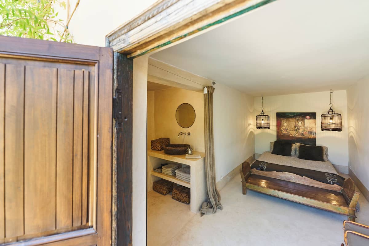 A bedroom with a wooden bed, a bedside table with a mirror, and a painting on the wall.