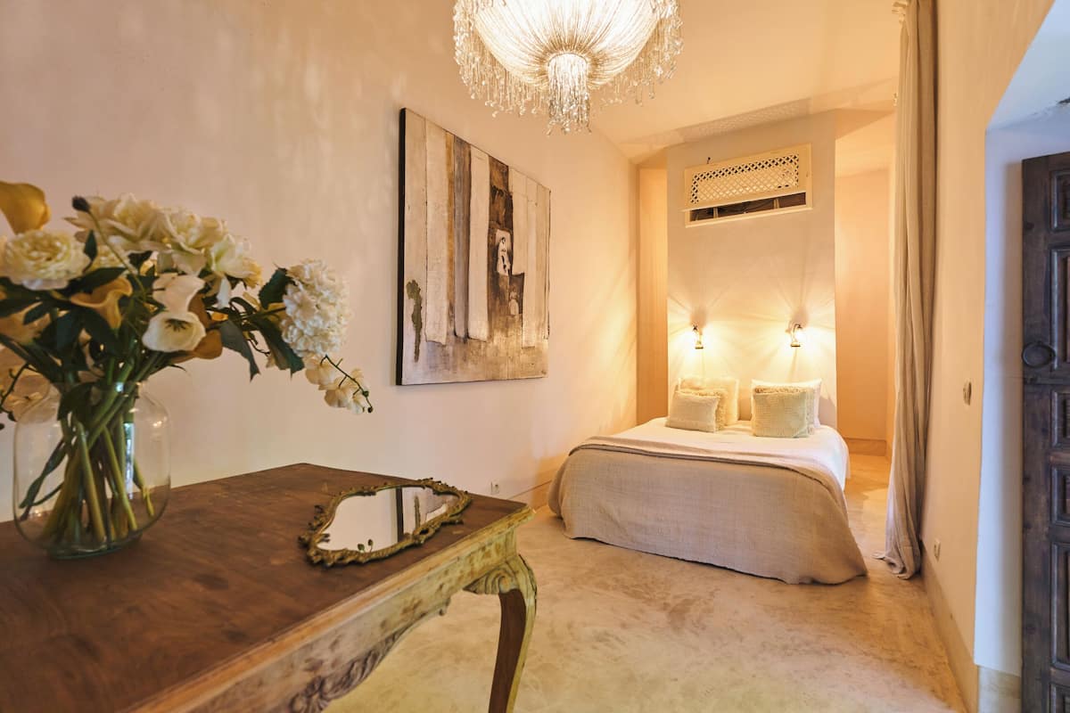 A bedroom with a bed, bedside lamps, a vase with flowers, and a chandelier.