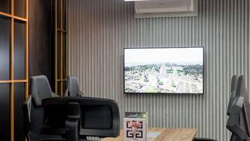 A modern conference room with a large table, black office chairs, a mounted TV displaying a cityscape, and a unique ceiling light fixture.