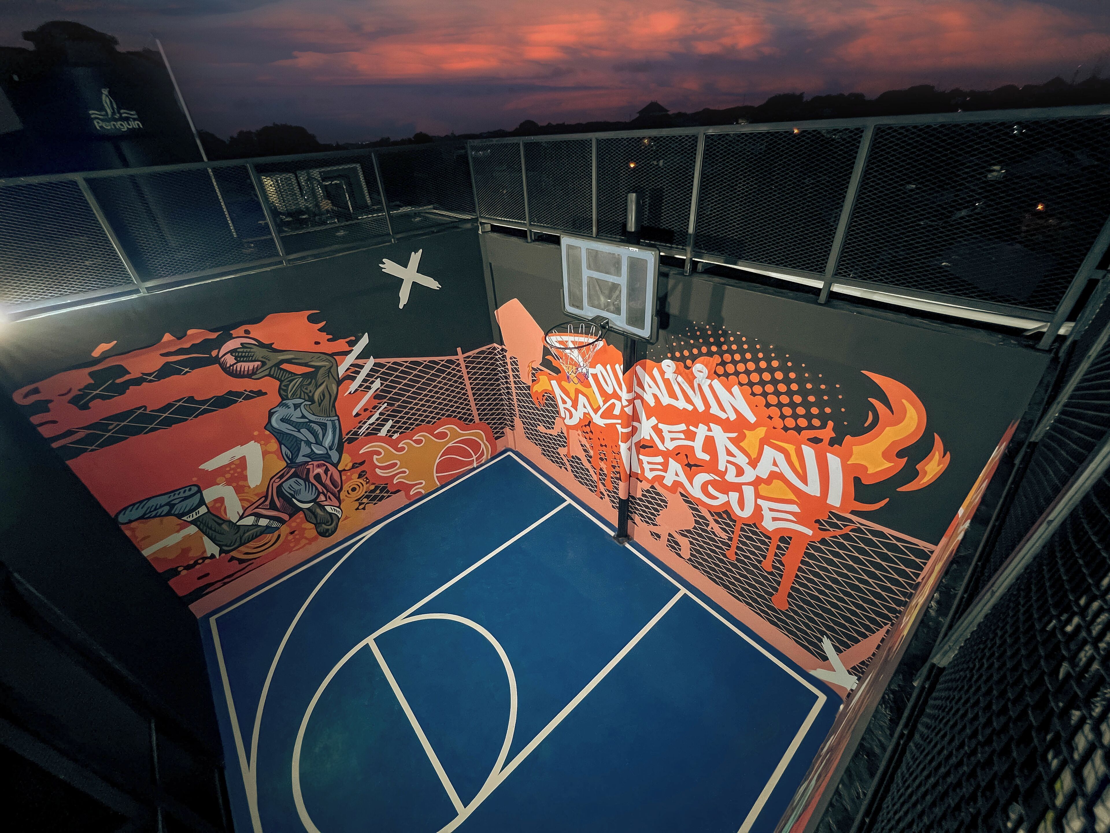 An outdoor basketball court with a mural, a basketball hoop, and a chain-link fence.