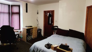 A bedroom with a bed, a desk, a chair, a door, and a window with curtains.