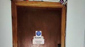 A wooden door with a sign that reads "ROOM 1 Please Ring The Bell!!" and a "Fire door Keep locked shut" sign.