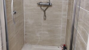 A glass-enclosed shower stall with a handheld showerhead and a fixed overhead showerhead.