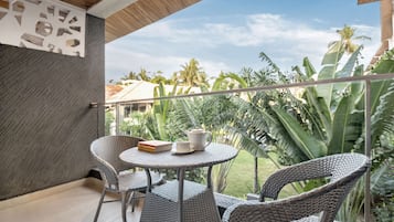 A balcony with wicker chairs, a small table, and a view of tropical vegetation.