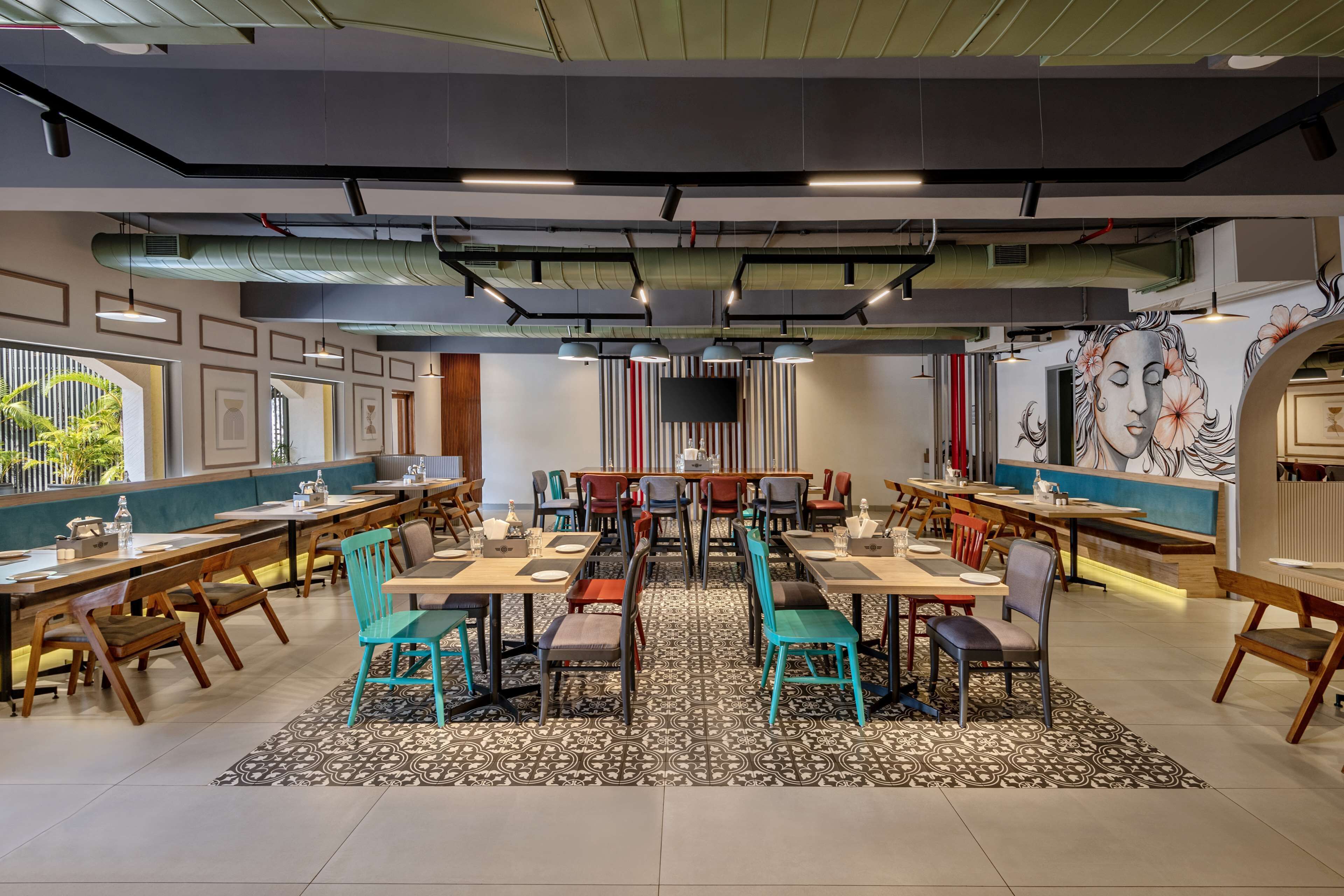 A restaurant with multiple dining tables and chairs, a patterned floor, and a large mural on the wall.