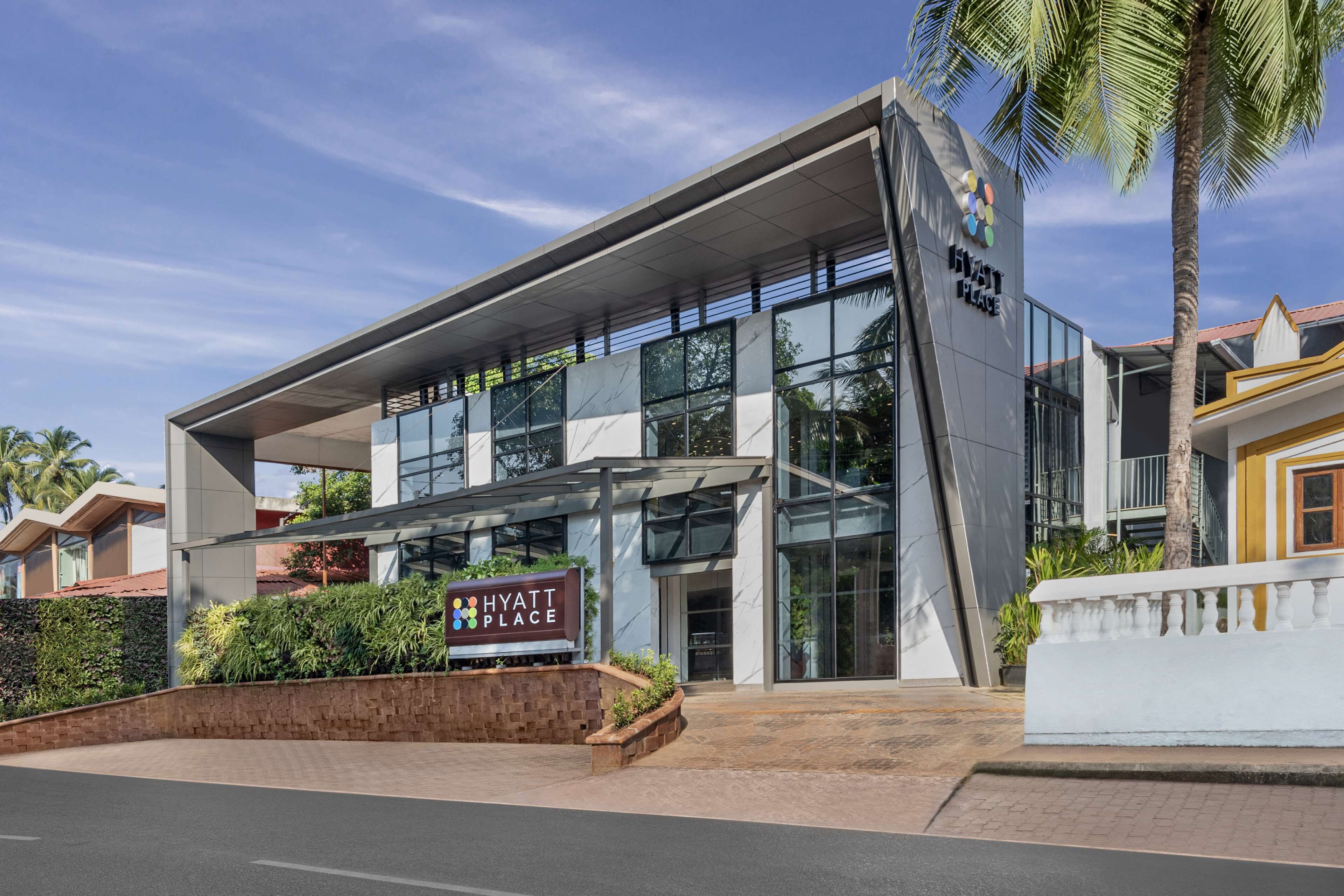 A modern hotel with a glass facade, a signboard, and a landscaped entrance.