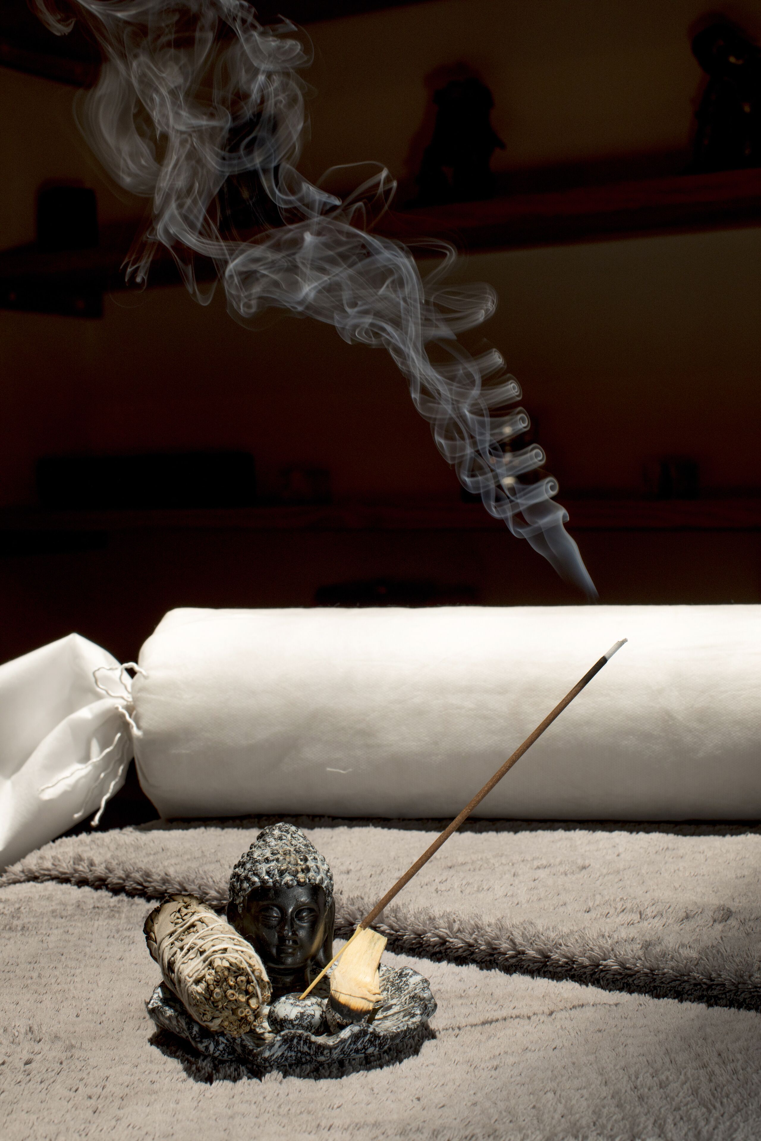 A room with a large white cylindrical object, a wooden stick, and a small Buddha statue on a textured surface.