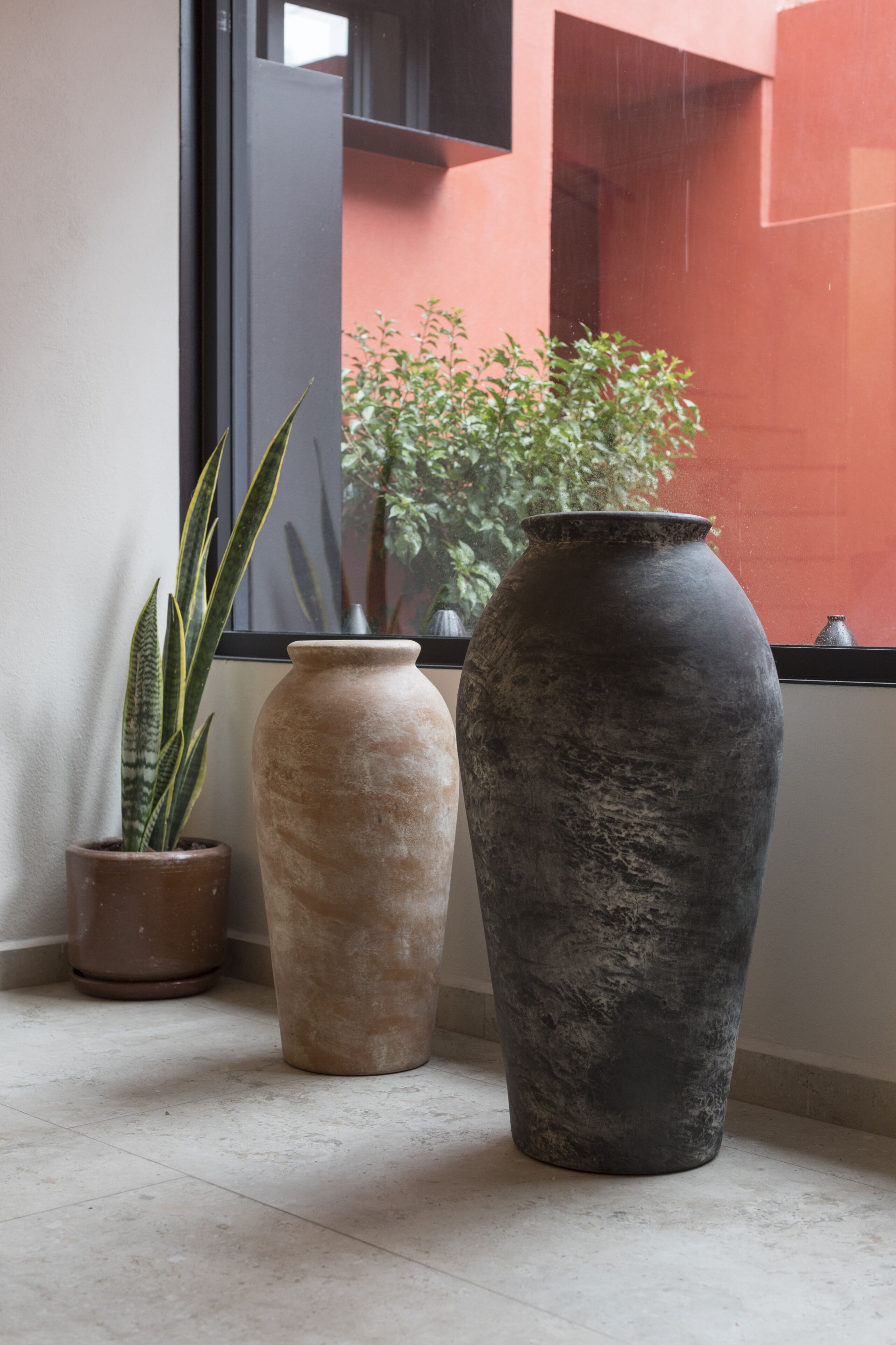Three large vases on a tiled floor near a window.