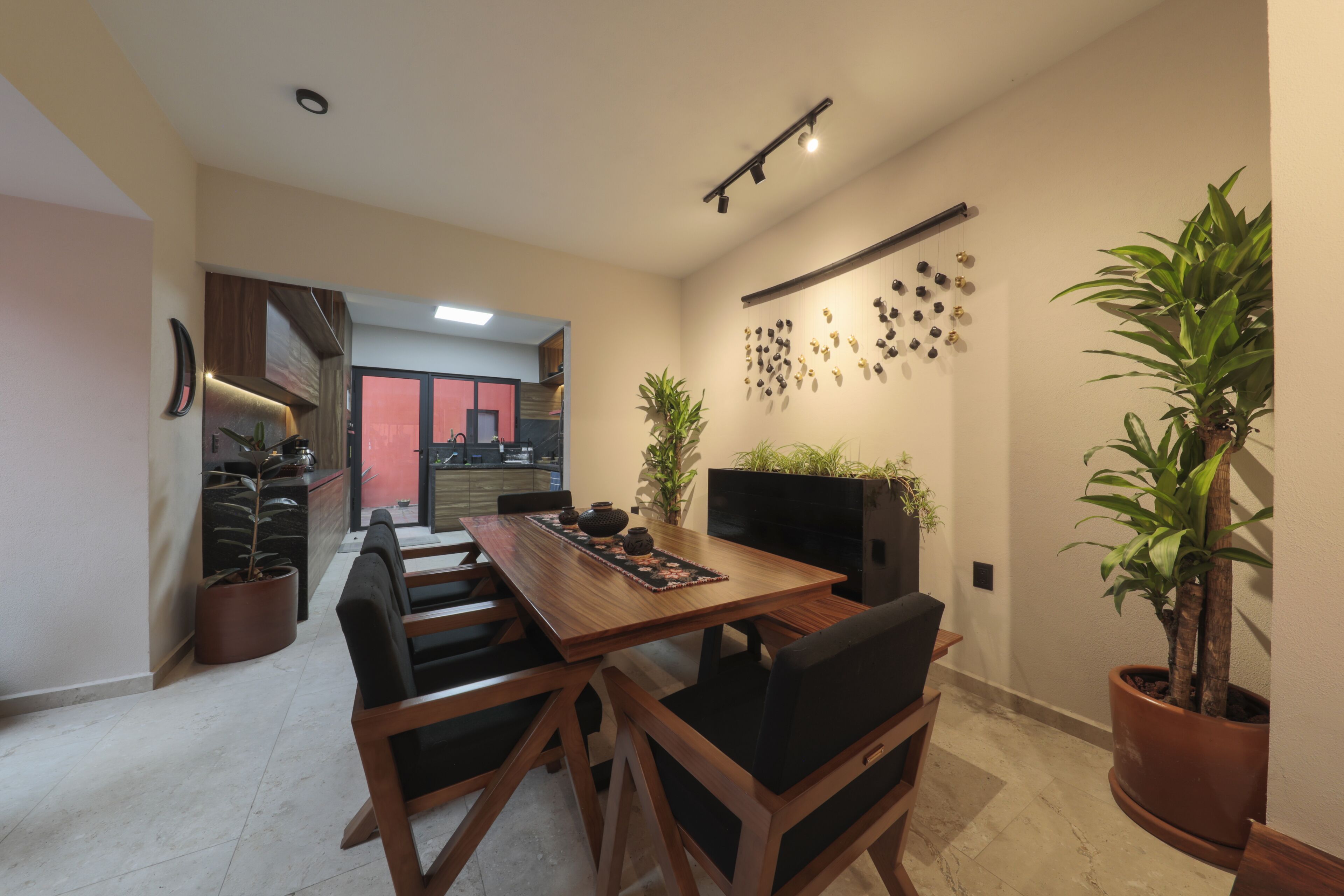Un coin repas avec une table en bois, des chaises noires et des plantes en pot. Un téléviseur est fixé au mur et un luminaire est suspendu au plafond.