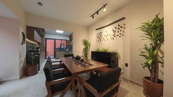 Un coin repas avec une table en bois, des chaises noires et des plantes en pot. Un téléviseur est fixé au mur et un luminaire est suspendu au plafond.