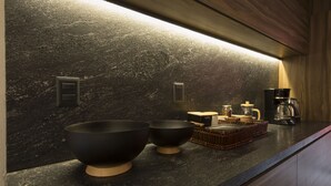 A modern kitchen with dark granite countertops, two black bowls, a coffee maker, and a basket of bread. - Casa Tonal (Mexico City)