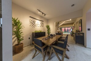 Un espace de salle à manger moderne, avec une table et des chaises en bois, des plantes en pot et un luminaire fixé au mur.