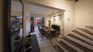 A modern kitchen with a dining area, wooden staircase, and a view into the living room. - Casa Tonal (Mexico City)