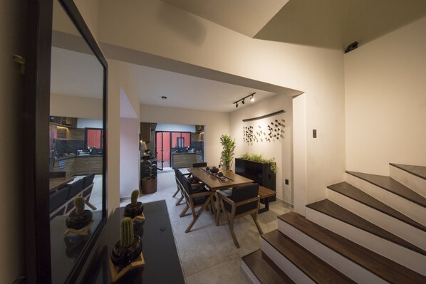 A modern kitchen with a dining area, wooden staircase, and a view into the living room. - Casa Tonal (Mexico City)