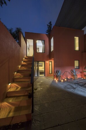 Un bâtiment moderne avec un escalier menant à l’entrée, des plantes en pot et un ciel dégagé.