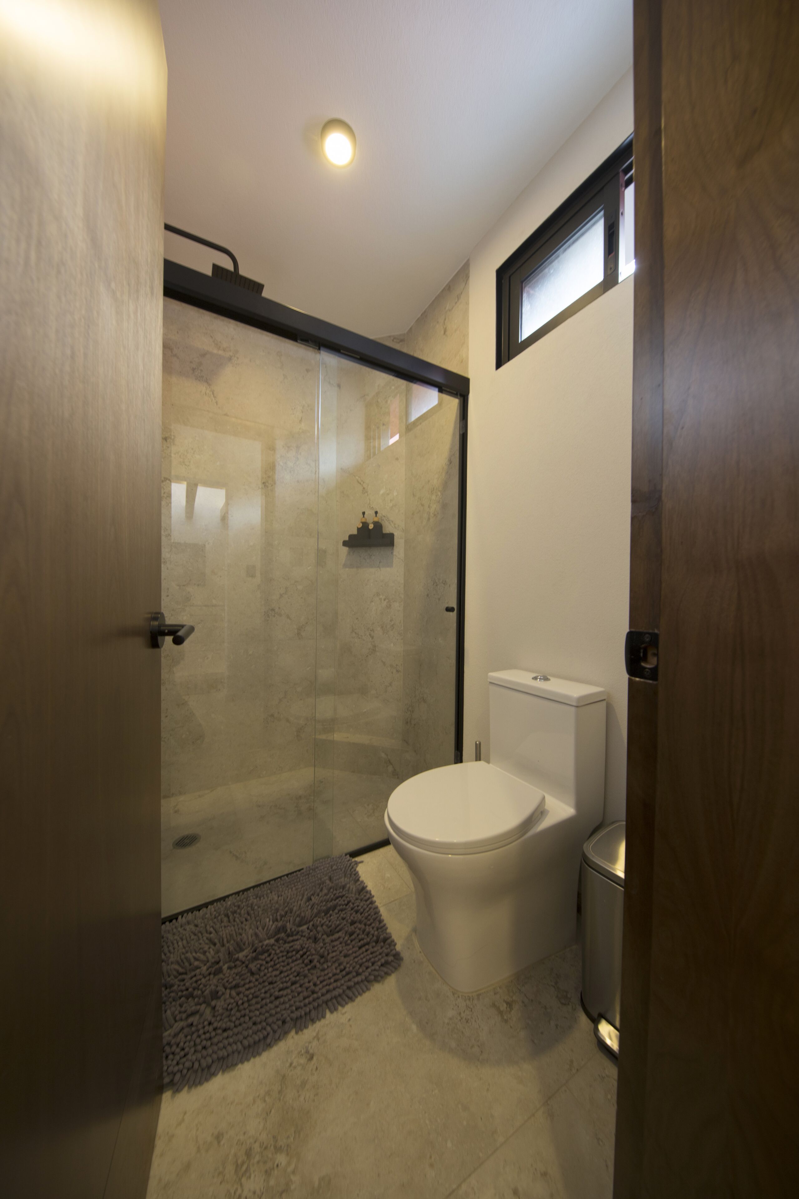 Un baño moderno con ducha de vidrio, inodoro y cubo de basura.