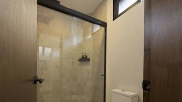 Un baño moderno con ducha de vidrio, inodoro y cubo de basura.