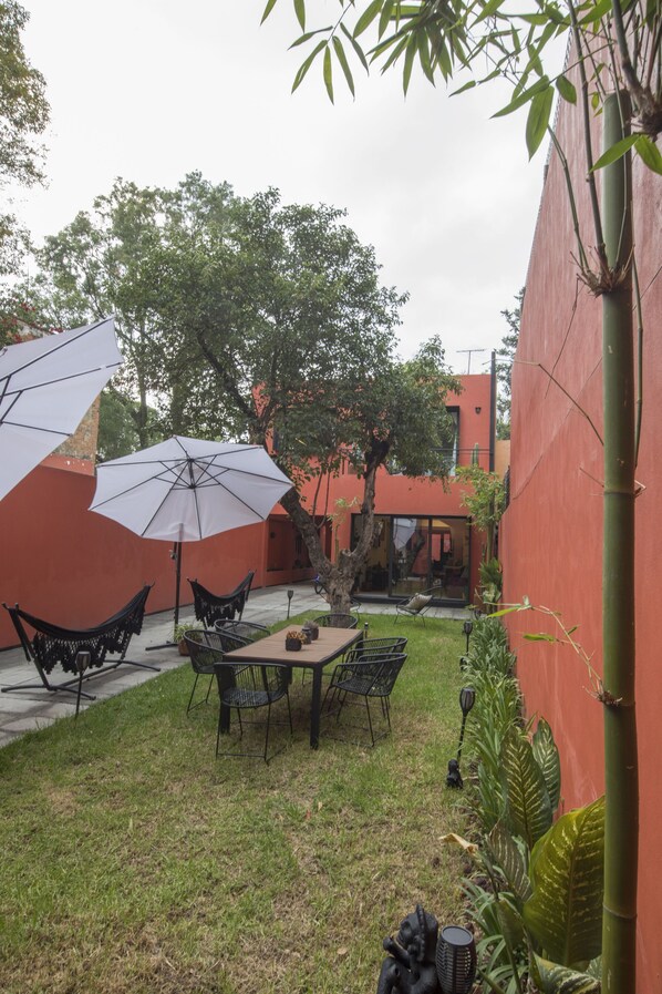Un patio con una mesa, sillas, dos sombrillas grandes y una hamaca.