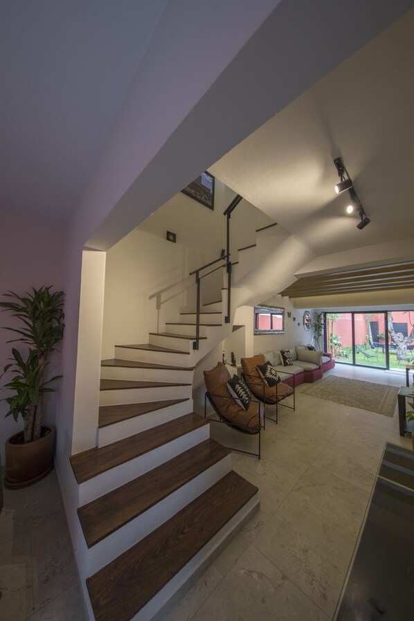 A modern interior with a staircase leading to a balcony, a seating area with cushions, and a potted plant. - Casa Tonal (Mexico City)