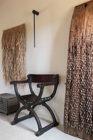 Un banco rústico de madera con estructura metálica, un tapiz de pared tejido y una puerta de madera con un diseño único.