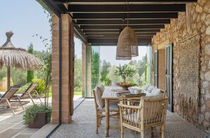 Un espacio de estar al aire libre cubierto, con una mesa, sillas y una lámpara colgante.