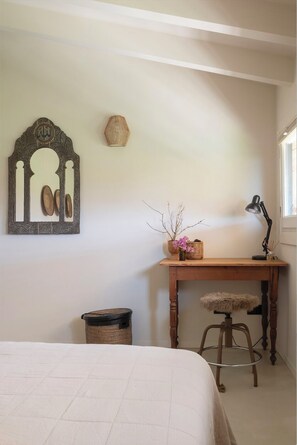 Un dormitorio con una cama, un escritorio de madera, un taburete, un cesto de basura y decoración en la pared.