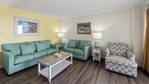 A living room with two green sofas, a patterned armchair, a wooden coffee table, and two side tables with lamps.