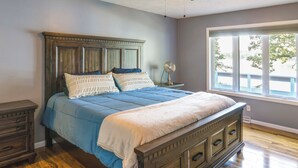A bedroom with a wooden bed, a nightstand, a dresser, and a window with a view of trees.