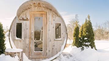 Une cabane en bois de forme sphérique, dotée d’une porte et de deux fenêtres, entourée de neige et d’arbres.