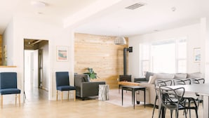 Een ruime woonkamer met een houten accentmuur, een bank, een eettafel met stoelen en een open haard.