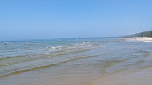Een strand met helder water, een zandstrand en een verre kustlijn met gebouwen.