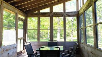 Un espace extérieur abrité, doté d’un plafond en bois et de grandes fenêtres, d’une table en verre et de quatre chaises.