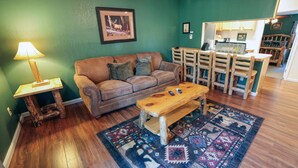 Una sala de estar acogedora con un sofá de cuero marrón, una mesa de centro de madera, un tapete estampado y un comedor con sillas y mesa de madera.