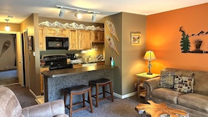 A modern kitchen with wooden cabinets, a central island, and a dining area with a sofa and coffee table. - Fawn Valley Inn: 284 1 Bedroom Condo (Estes Park)