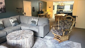 A living room with a grey sofa, a round coffee table, and a wooden chair with patterned cushions. - Fawn Valley Inn: 302 2 Bedroom Condo (Estes Park)
