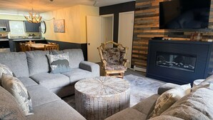 A living room with a sectional sofa, a round coffee table, a fireplace, and a television mounted on a wooden wall. - Fawn Valley Inn: 302 2 Bedroom Condo (Estes Park)