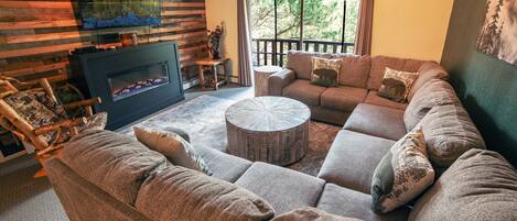 A cozy living room with a fireplace, a large sectional sofa, and a round coffee table.