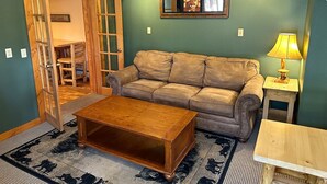 A cozy living room with a leather sofa, wooden coffee table, and a small side table with a lamp. - Timber Creek Chalets: 10b 1 Bedroom Chalet (Estes Park)