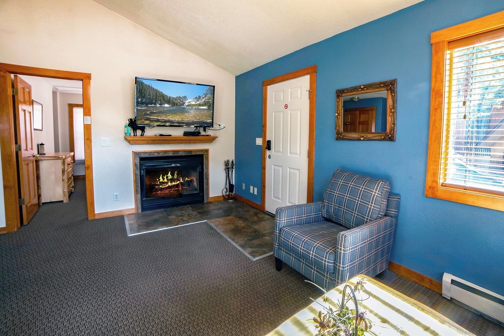 A living room with a fireplace, a television, a blue wall, and a plaid armchair.