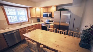 A kitchen with wooden cabinets, stainless steel appliances, a wooden dining table, and a window with blinds. - Timber Creek Chalets: 8 3 Bedroom Chalet (Estes Park)