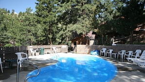 A swimming pool with a diving board, surrounded by white plastic chairs and a stone wall. - Timber Creek Chalets: 8 3 Bedroom Chalet (Estes Park)