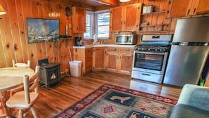 Une cuisine chaleureuse, aménagée dans le style d’un chalet, avec des murs en bois, une cuisinière, un four, un four à micro-ondes et un coin repas comprenant une table et des chaises.