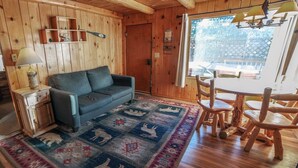 L’intérieur d’un chalet chaleureux, avec un canapé, un tapis à motifs animaliers, des meubles en bois et une fenêtre donnant sur la forêt.