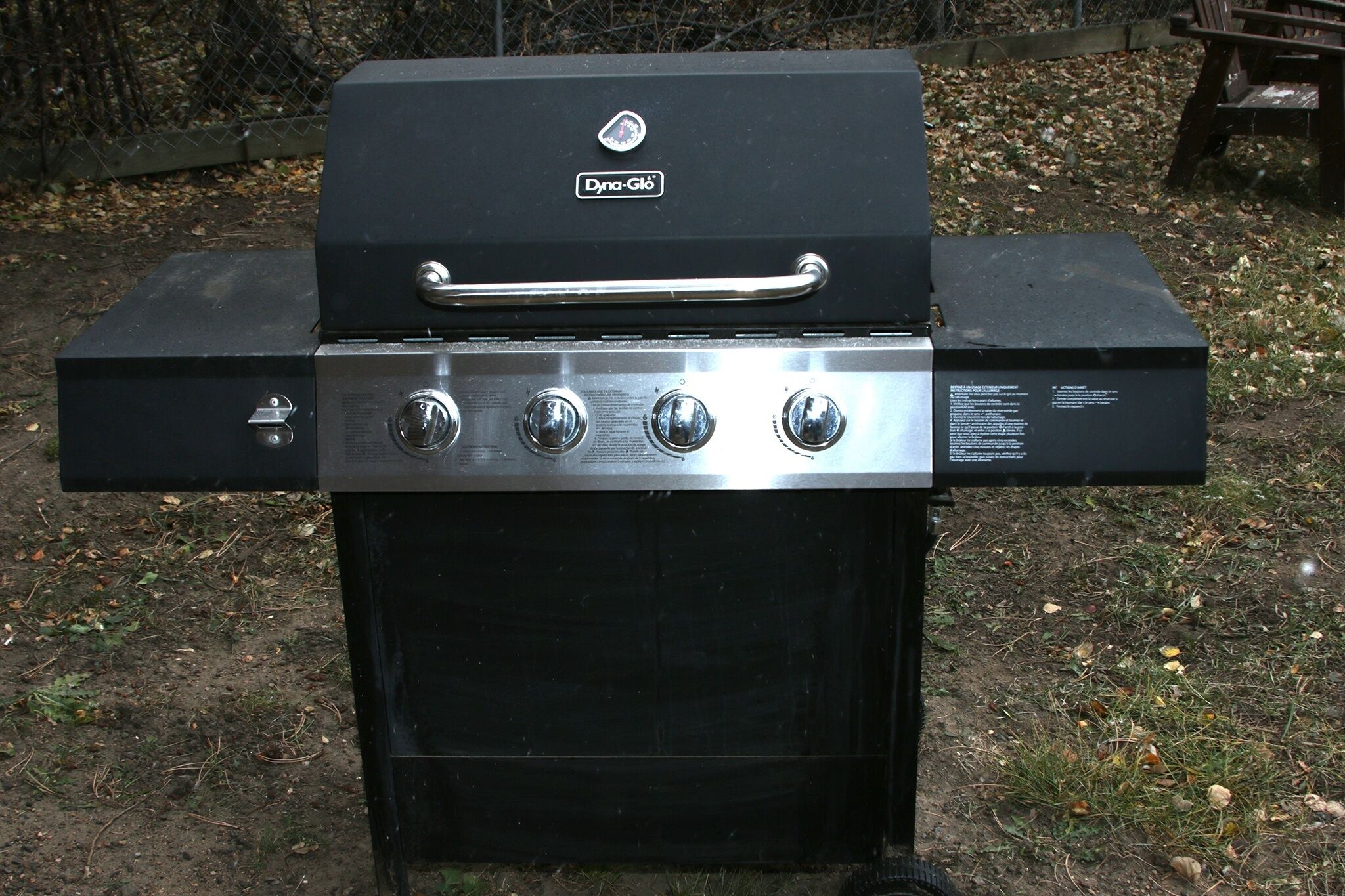 A black outdoor grill with a handle and four control knobs.