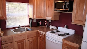 Une cuisine de taille réduite, avec des meubles de rangement en bois, une cuisinière blanche, un four à micro-ondes et un évier.