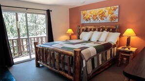 Une chambre à coucher avec un lit en bois, deux lampes de chevet, une grande fenêtre donnant sur des arbres et un tableau accroché au mur.