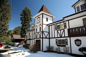 Un edificio in stile Tudor tradizionale con una torre e un orologio in evidenza, circondato da terreno e alberi coperti di neve.