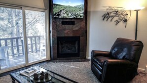 A living room with a fireplace, a leather chair, and a glass coffee table. - Fawn Valley Inn: 292 1 Bedroom Apts (Estes Park)
