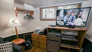 Un espacio habitable compacto con televisor, muebles de madera, una mesita pequeña y un sofá con un cojín estampado.