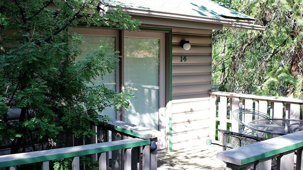 A wooden deck with a metal table and chairs, a door with a number, and surrounding greenery. - Sunnyside Knoll: 14 Studio (Estes Park)